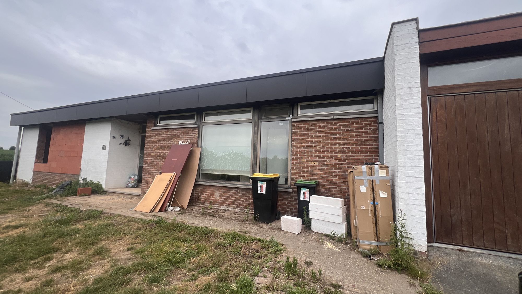De voorgevel van de bungalow in Pittem voor de werken, in rode baksteen met een bruine houten garagepoort
