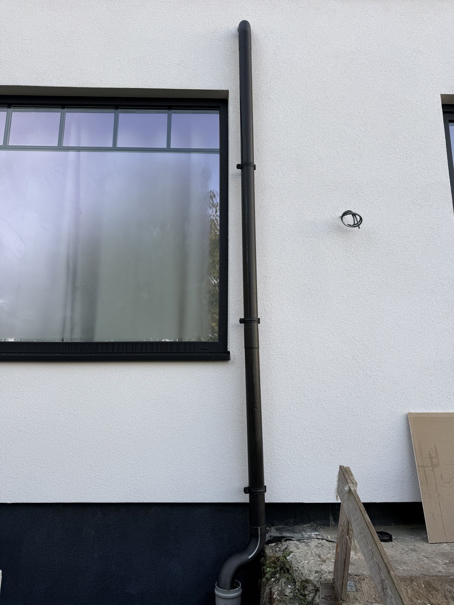 Een raam in de witte crepi in Pittem met de nieuwe zwarte regenpijp en de zwarte plint eronder