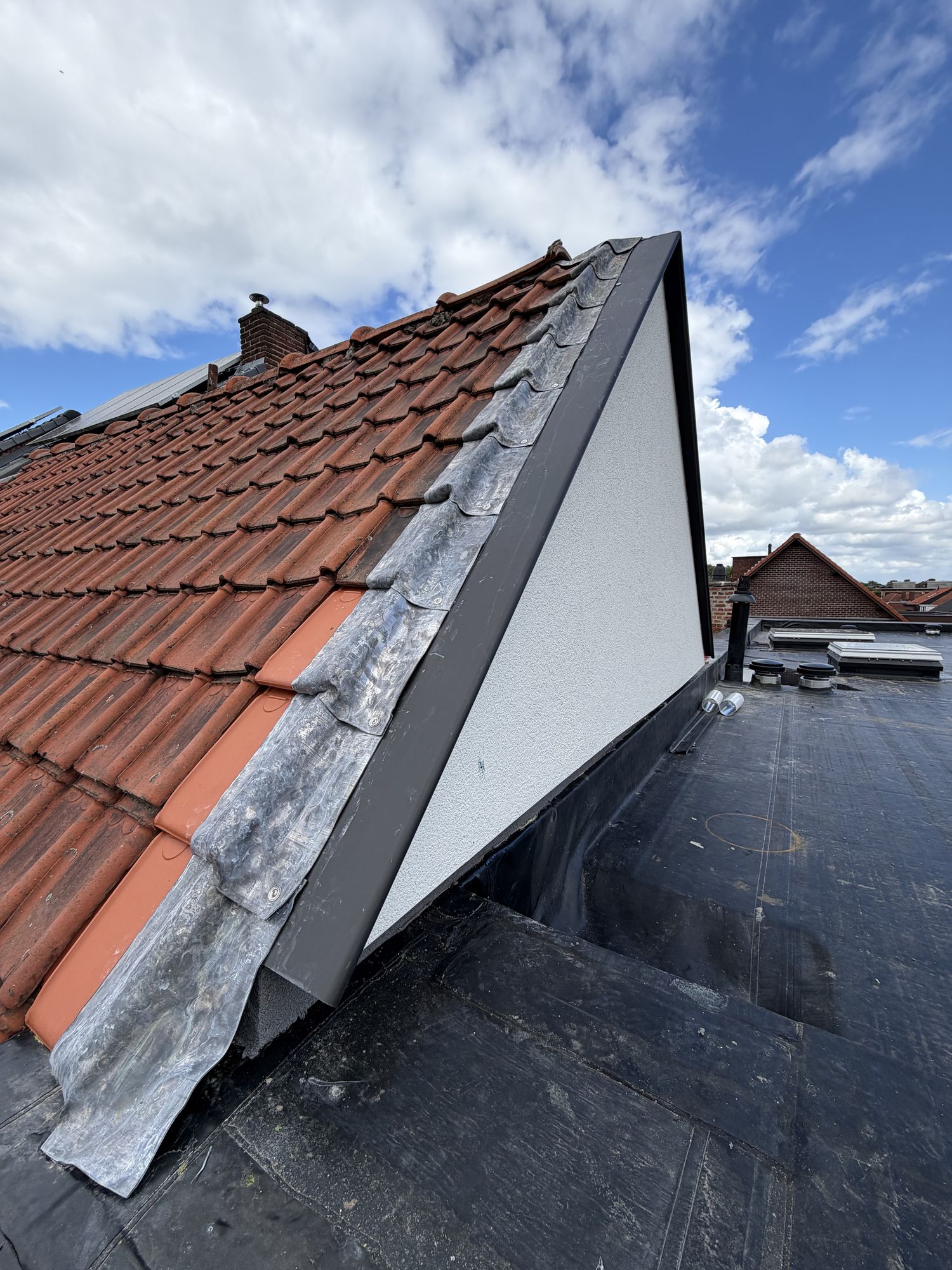 De aansluiting in Gent tussen het nieuwe platte dak en het pannendak van de buren, met zwart aluminium en witte crepi