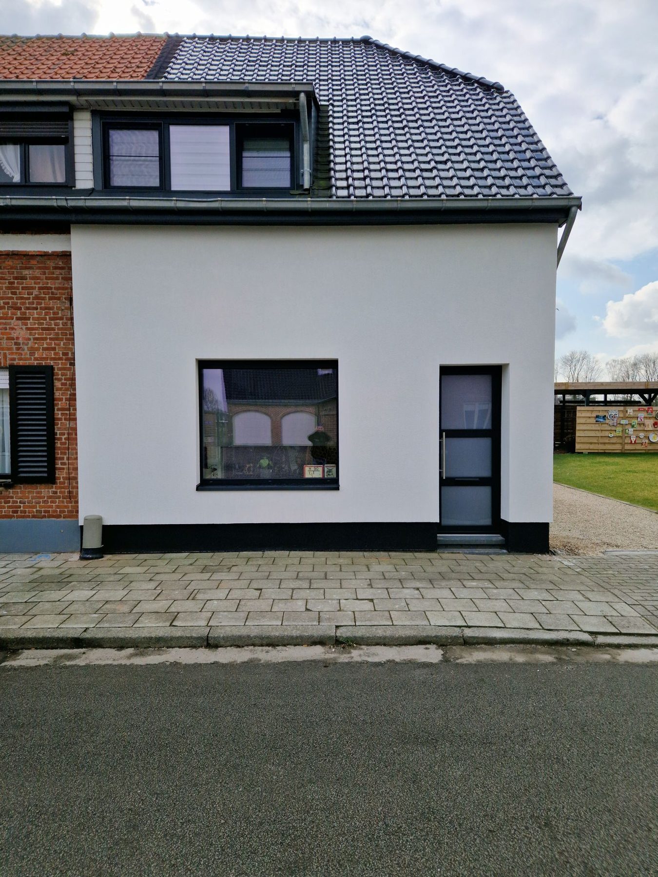 De afgewerkte gevel in Overmere met witte crepi, antracieten ramen en een nieuwe zijdeur