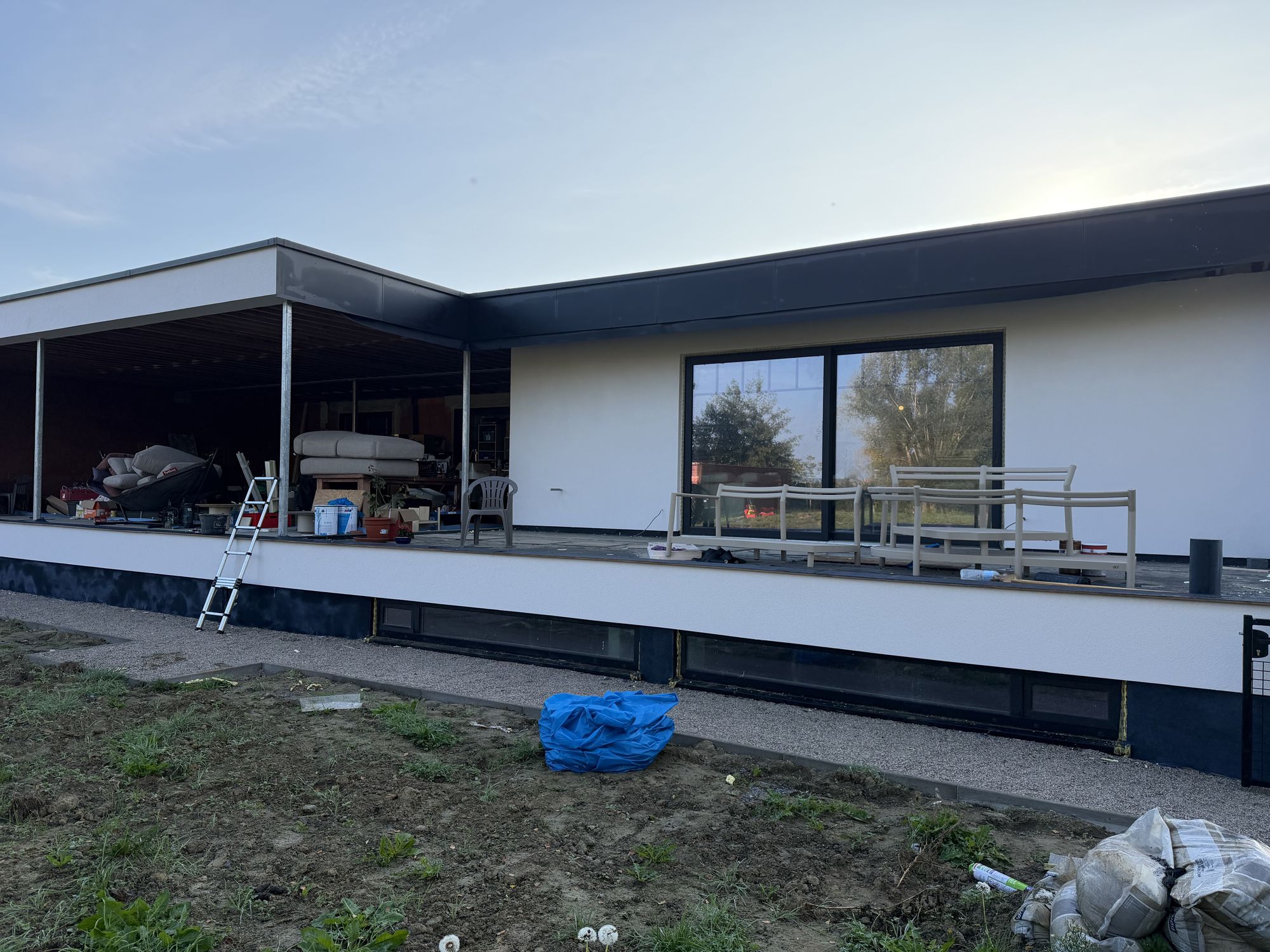 De lange witte terrasgevel met overkapping in Pittem in het avondlicht na de gevelisolatie