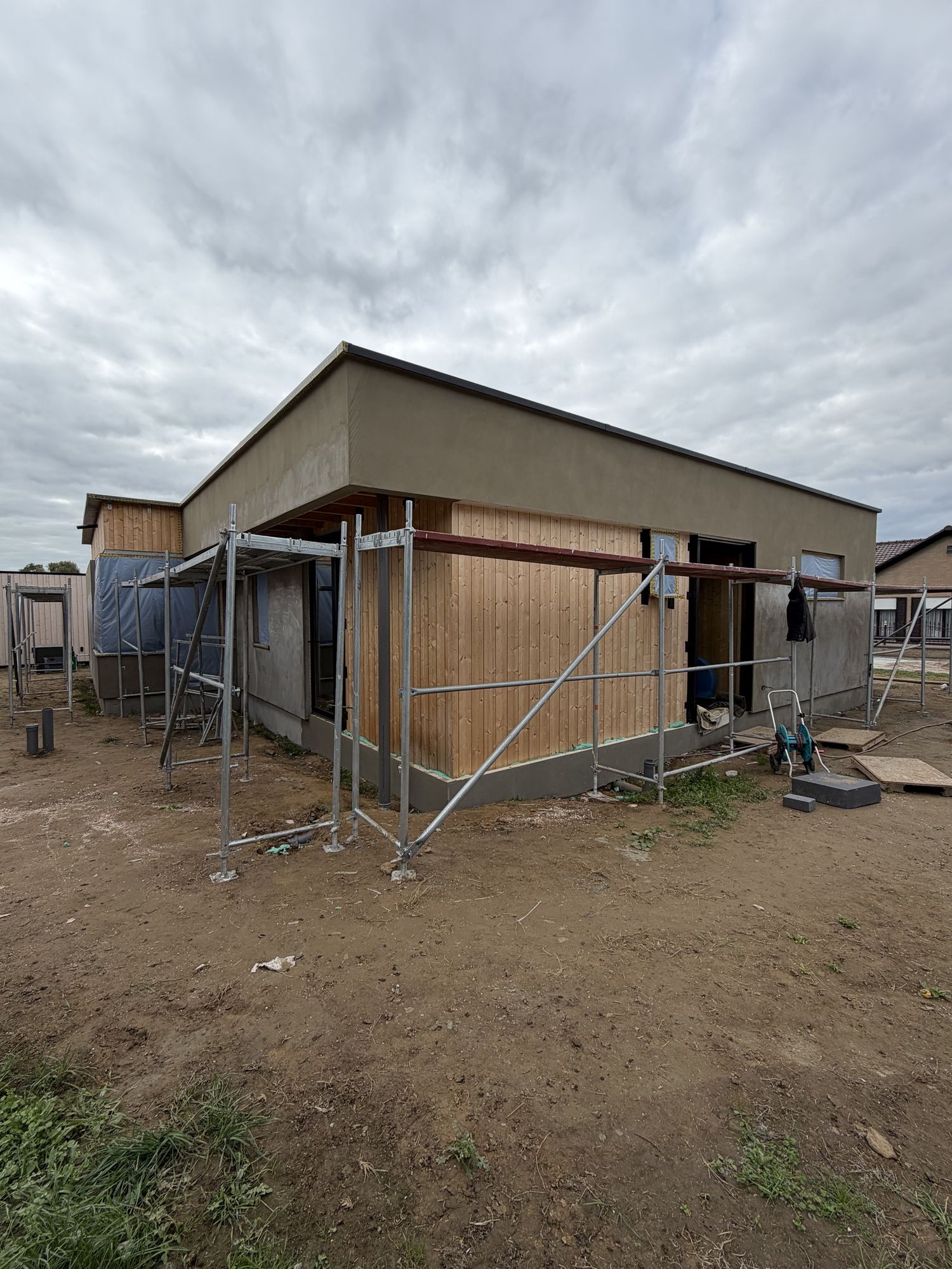 De woning in Brakel halfweg de werken: links de basislaag op de nieuwe isolatie, rechts nog het houten gevelvlak, met de stelling ervoor