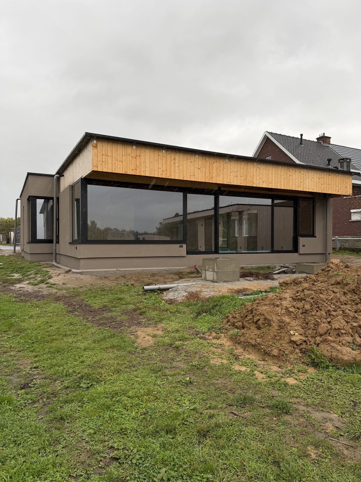 De achterzijde van de woning in Brakel na de werken, met een grote glaspartij, het houten overstek en taupe spuitkurk