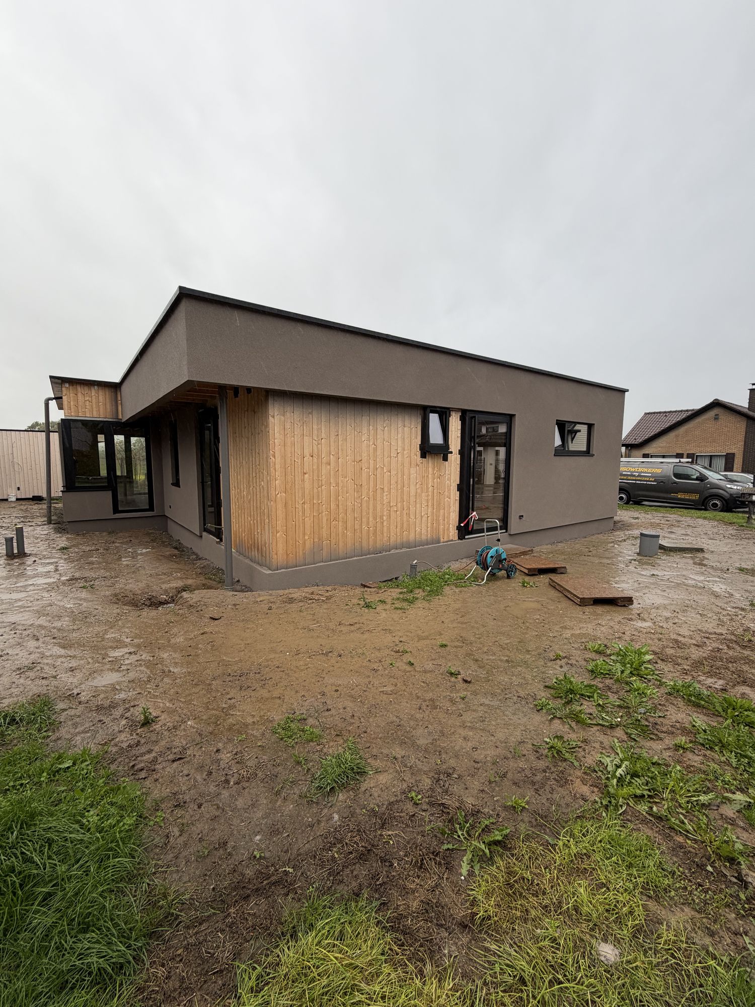 De voorzijde van de woning in Brakel na de werken, met taupe spuitkurk onder het dak en een houten vlak dat bewust in het zicht bleef