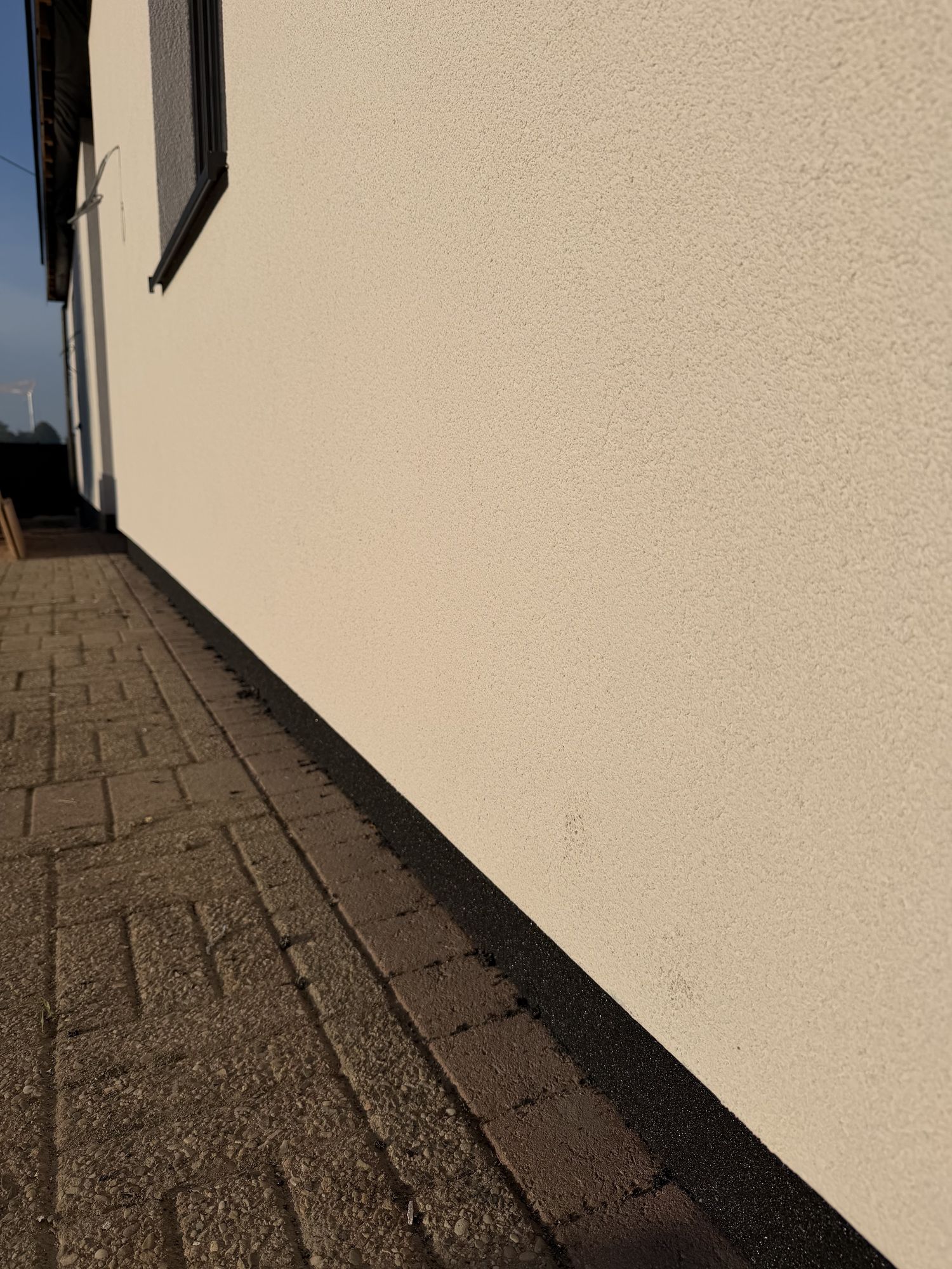 De zwarte gevelplint onder de witte crepi, net boven de klinkers, aan de bungalow in Pittem