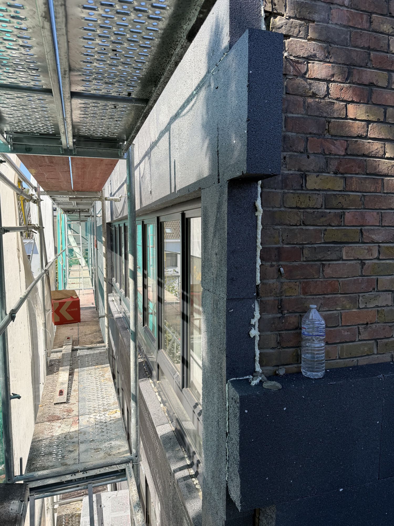 Grafietgrijze EPS-isolatieplaten tegen de bakstenen gevel van het hoekgebouw in Gent, gezien vanaf de stelling