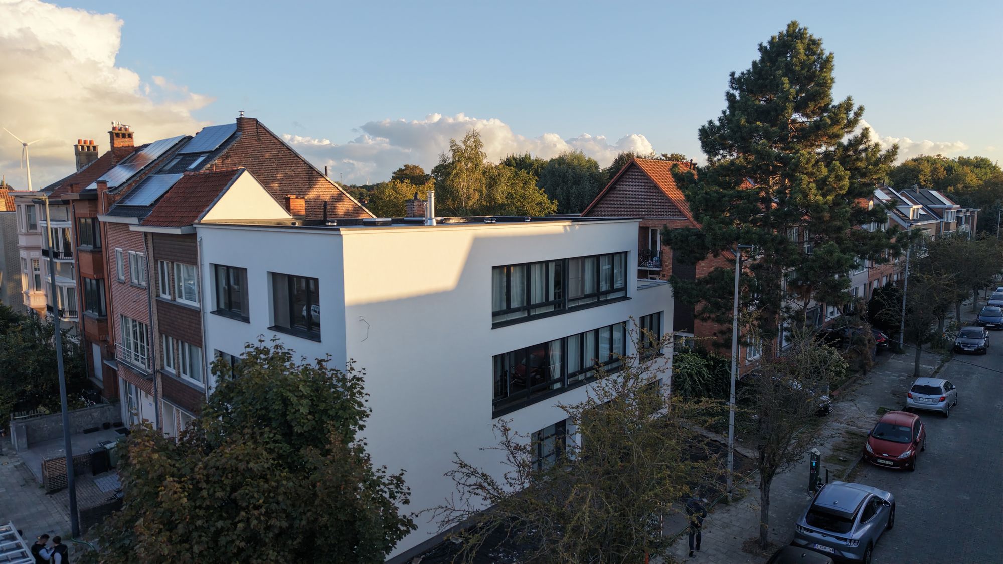 Het afgewerkte hoekgebouw in Gent in avondlicht, met witte crepi op drie gevels en een nieuw plat dak
