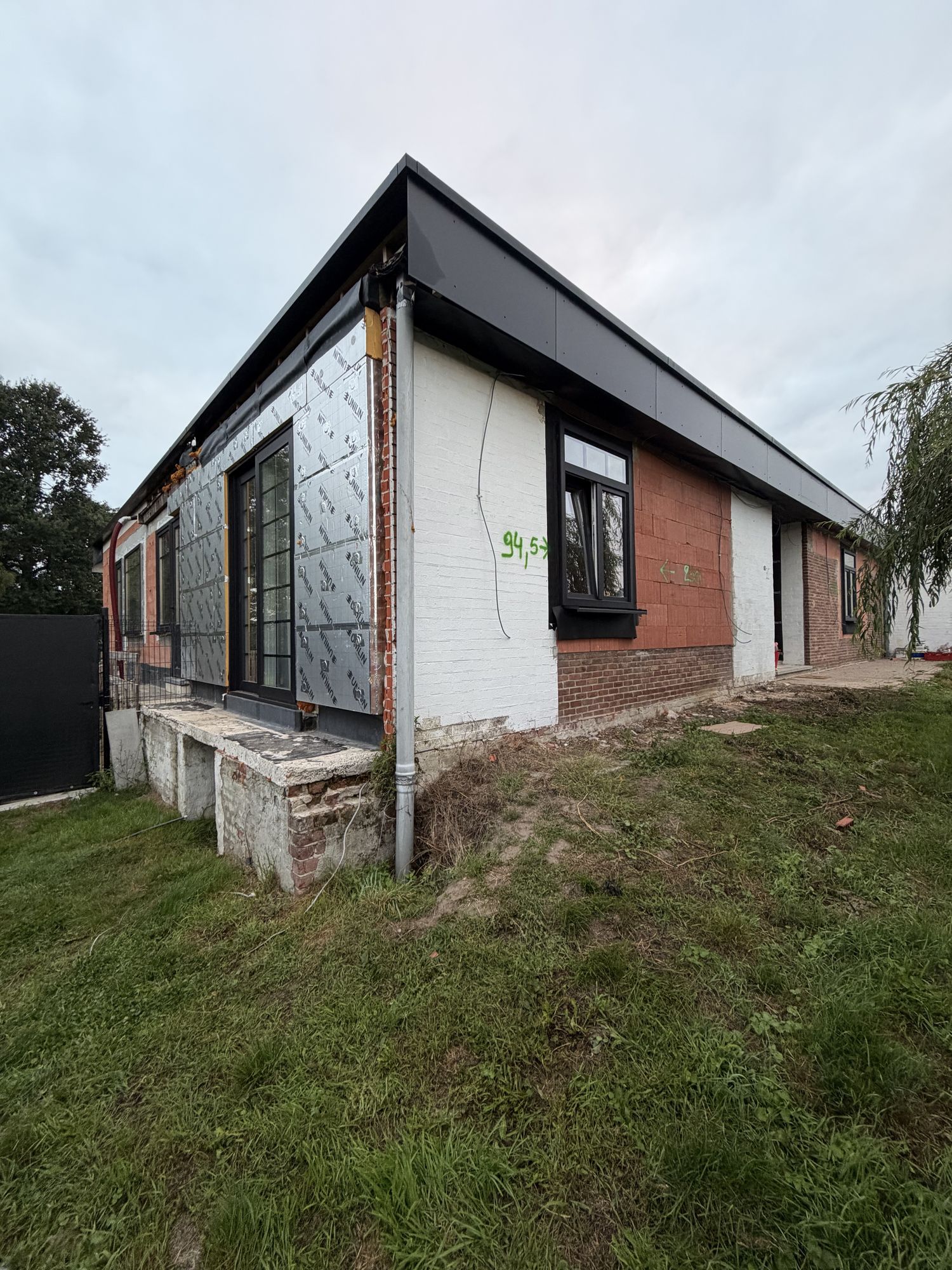 De hoek van de bungalow in Pittem bij de start van de werken, links nog de oude isolatieplaten en rechts de blote baksteen tot onder de dakrand