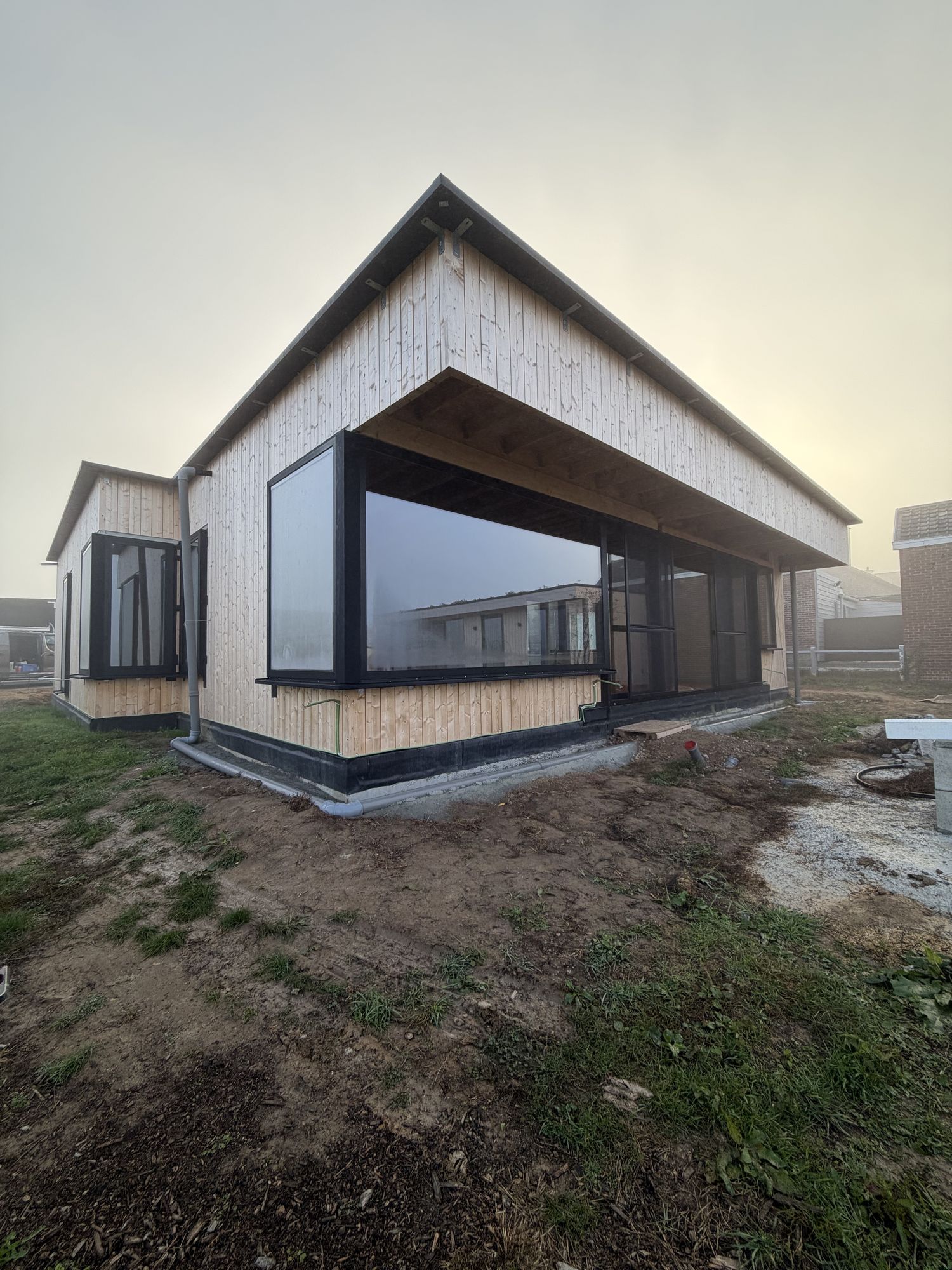 Dezelfde zijde van de woning in Brakel voor de werken, met verticale houten planken, een hoekraam en een zwarte plint