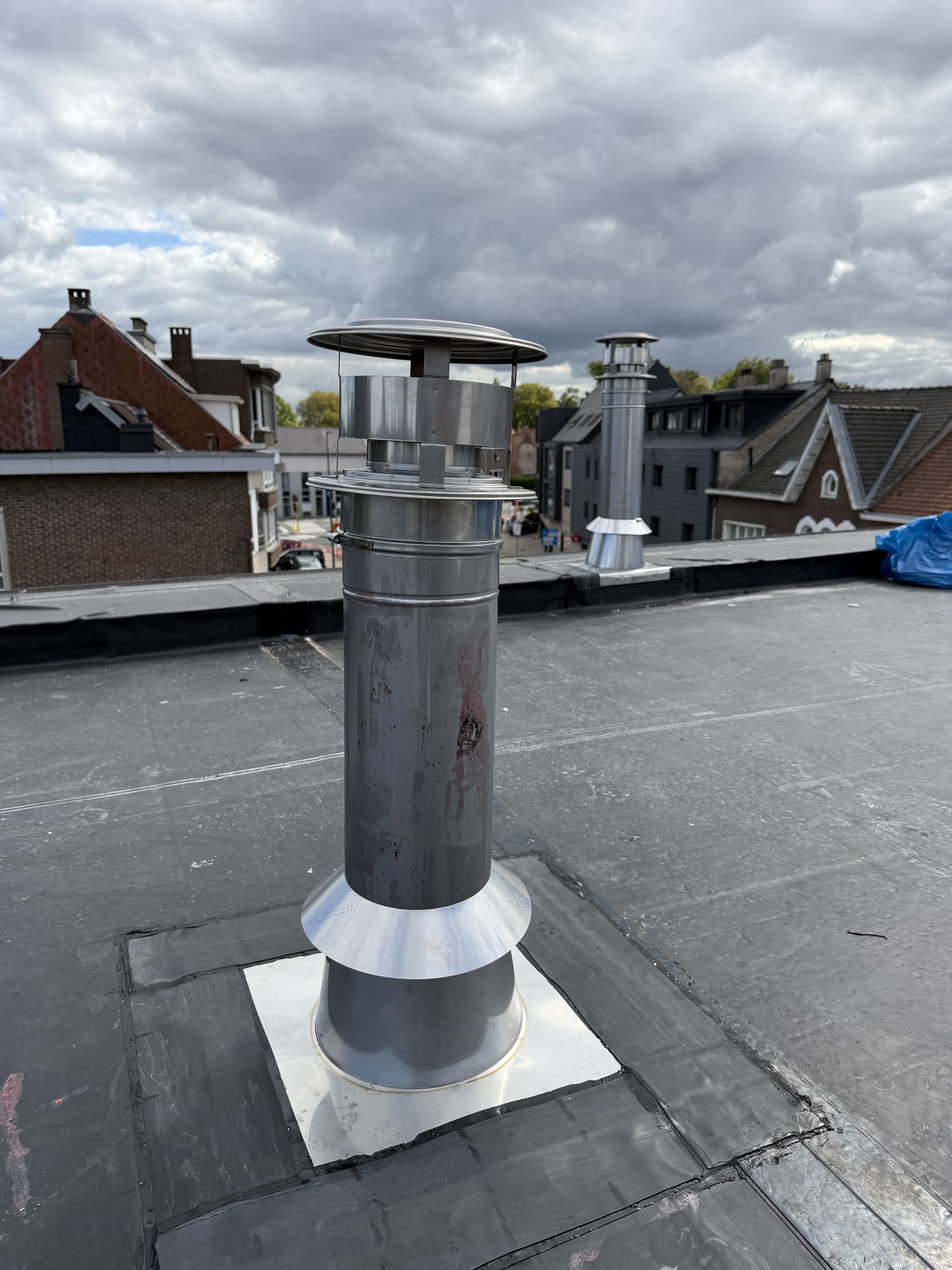 Een inox rookgasafvoer met rubberen kraag midden op het nieuwe EPDM-dak in Gent