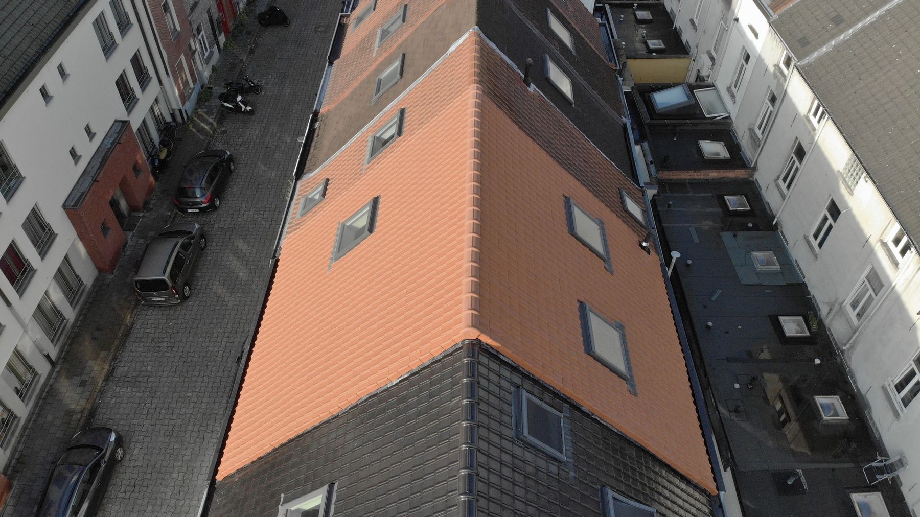Het nieuwe pannendak in Gent vanuit de lucht, met de straat en de donkere daken van de buren ernaast