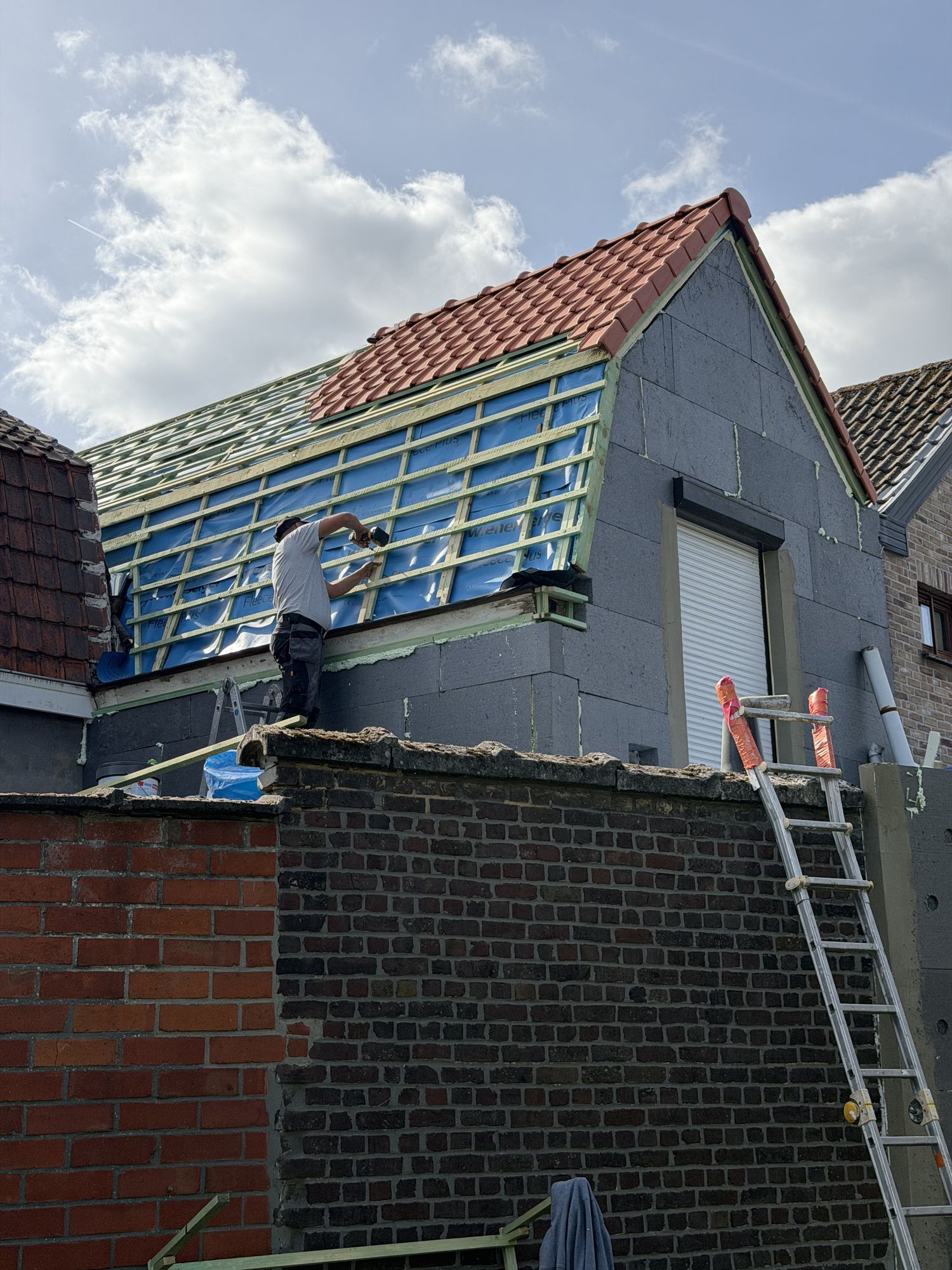 Dakwerker op de gevelspits in Oostakker, met het onderdak en de tengellatten van het sarkingdak naast de geïsoleerde gevel