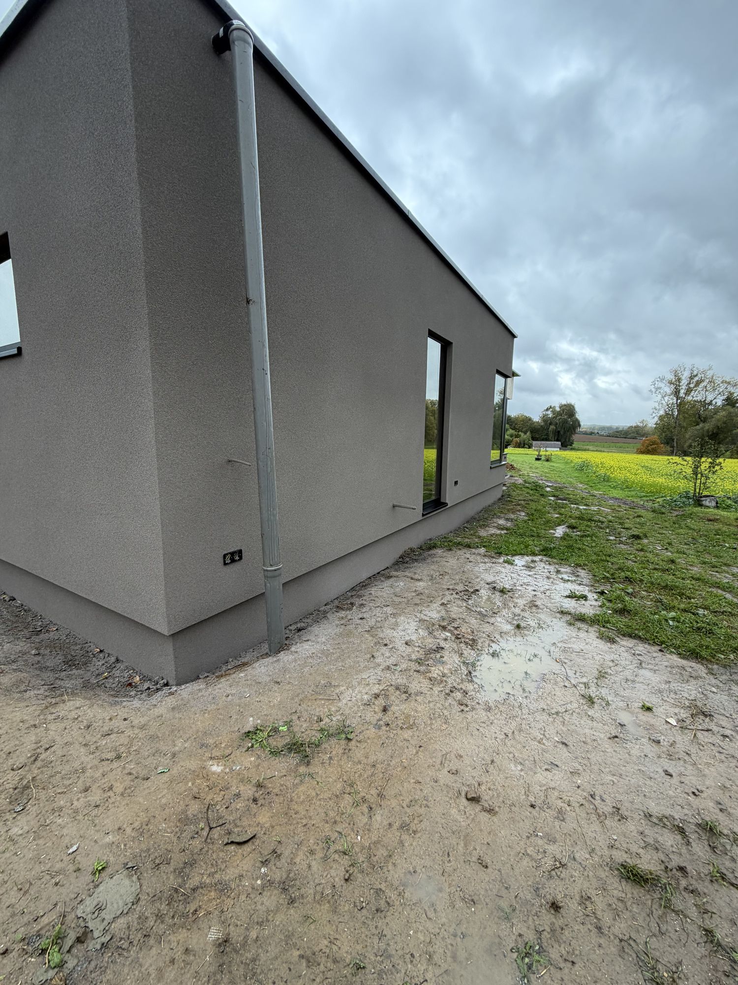 Een gevelhoek in Brakel na de werken, met de donkerdere plint onderaan en het open landschap op de achtergrond