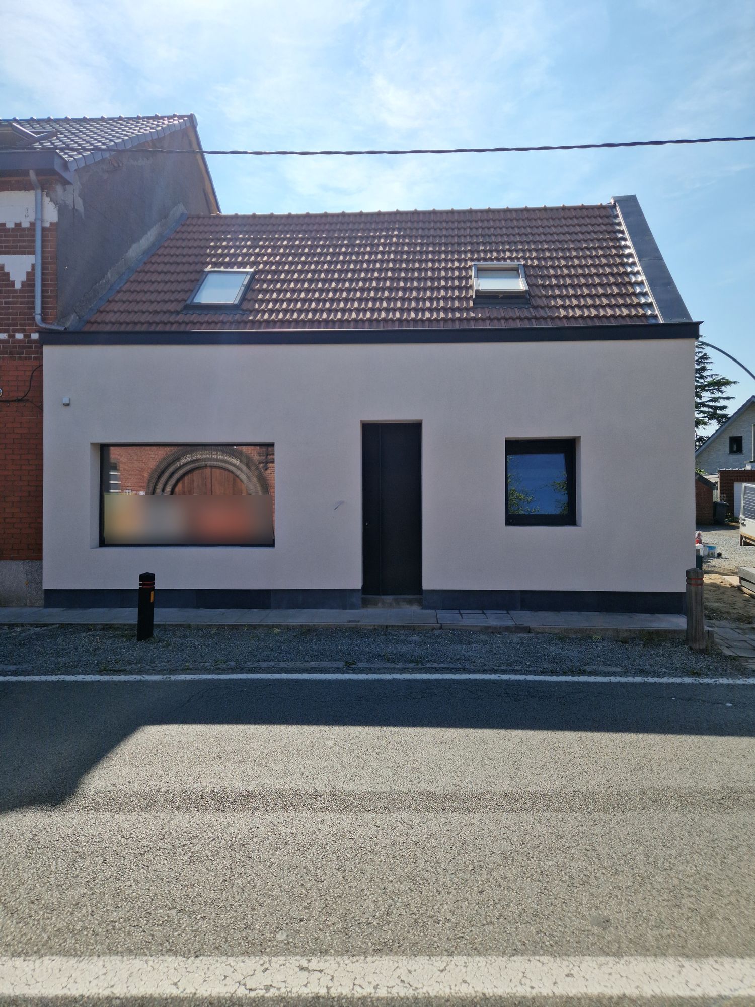 De voorgevel in Merelbeke na de gevelisolatie, afgewerkt met witte spuitkurk en een donkere plint