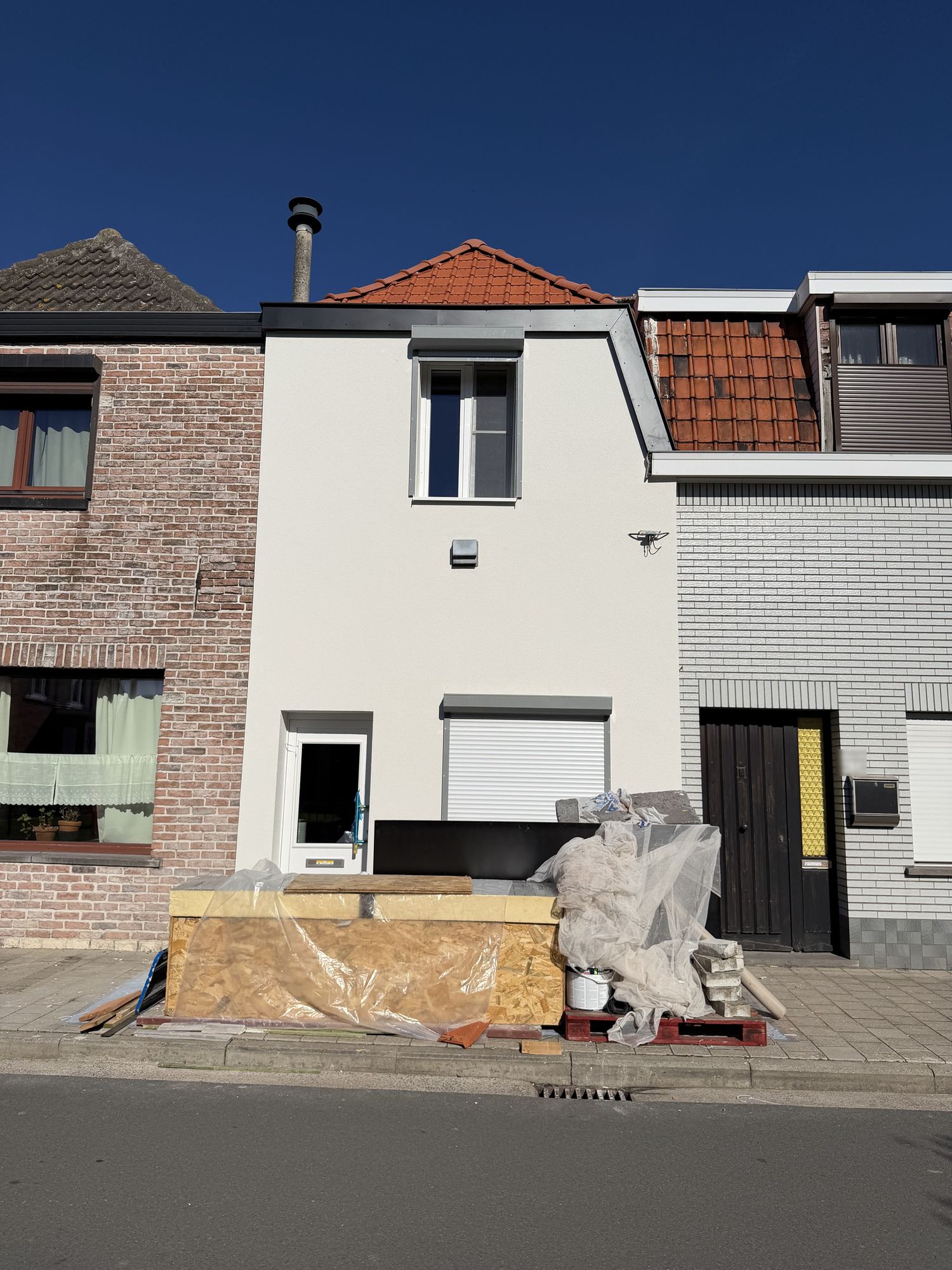 De voorgevel in Oostakker na de werken, witte crepi met een nieuw grijs rolluik en zwarte plint