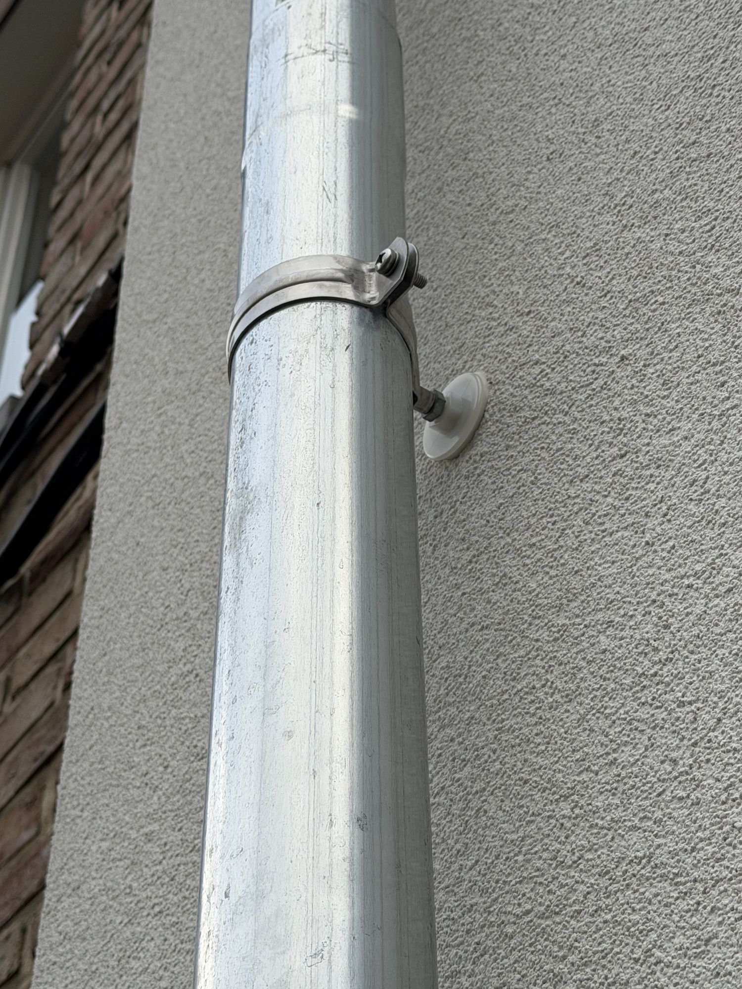 Nieuwe zinken regenpijp op de witte crepi van het hoekgebouw in Gent